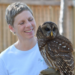 A woman smiles and looks at the owl perched on her gloved hand.